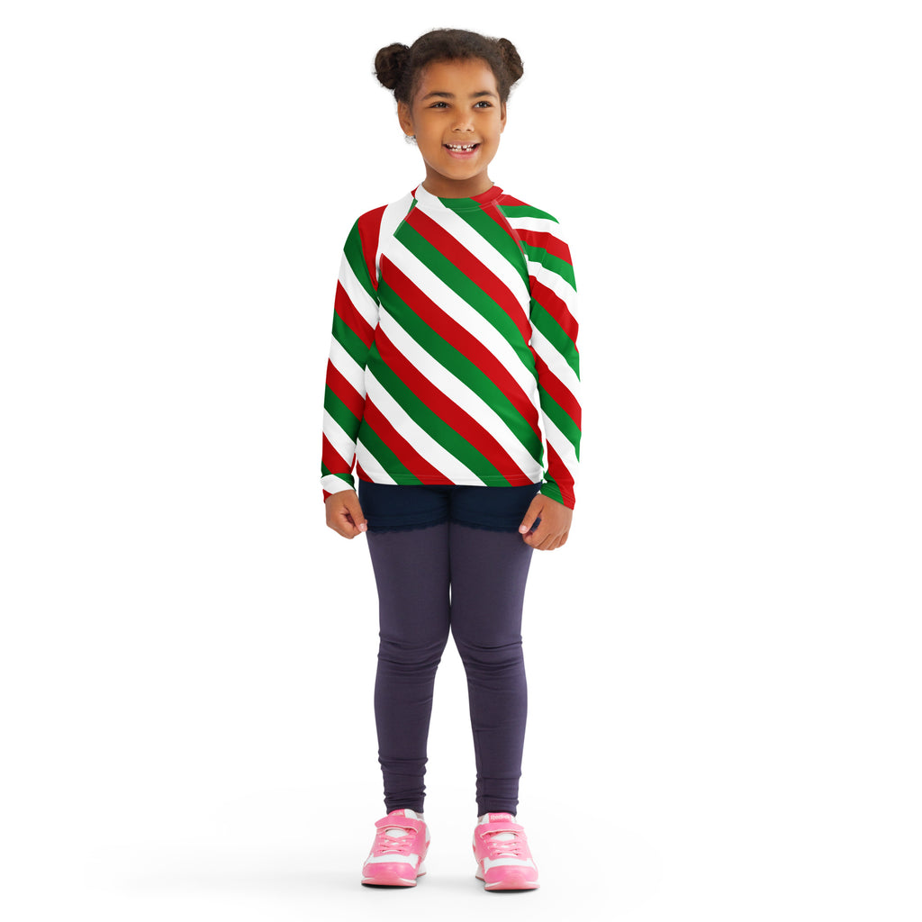 A child wearing a kids bold candy cane stripe christmas long sleeve rash guard swim shirt with UPF 50+ and red green white stripes
