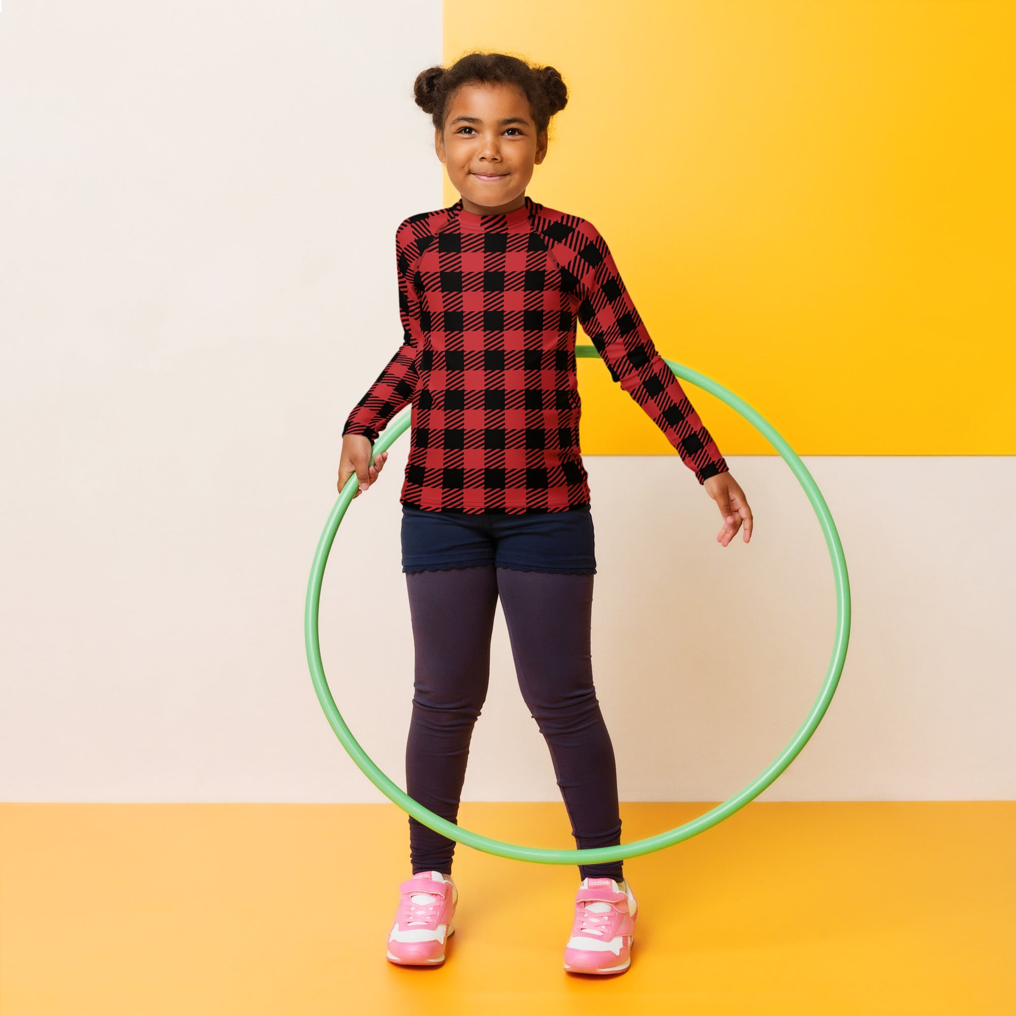 Green plastic hula hoop next to a kids red buffalo plaid christmas long sleeve rash guard swim shirt with upf 50+