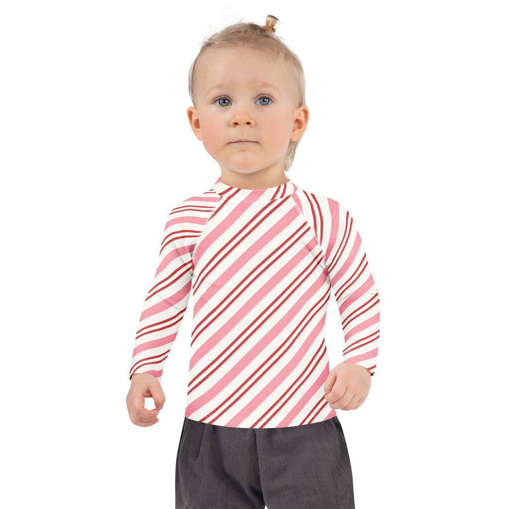 A child wearing a kids pink peppermint stripe Christmas long sleeve rash guard swim shirt with UPF 50+ diagonal stripes