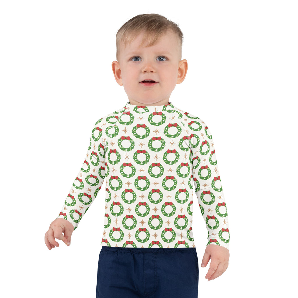 A child wearing a white kids christmas wreath long sleeve rash guard swim shirt with upf 50 plus and green wreaths
