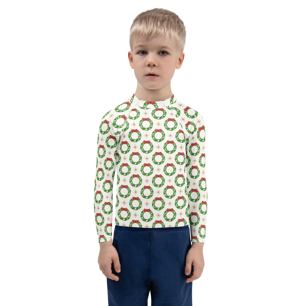 A child wearing a white kids christmas wreath long sleeve rash guard swim shirt with upf 50 plus and green wreaths