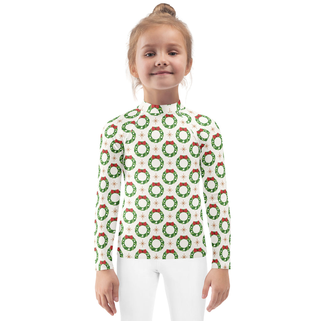 A child wearing a kids christmas wreath long sleeve rash guard swim shirt with upf 50 plus in white with green wreaths and red bows