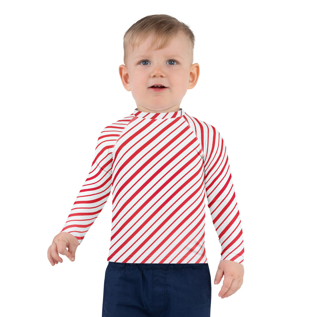 A child wearing a kids red and white candy cane striped long sleeve rash guard swim shirt with UPF 50+ protection
