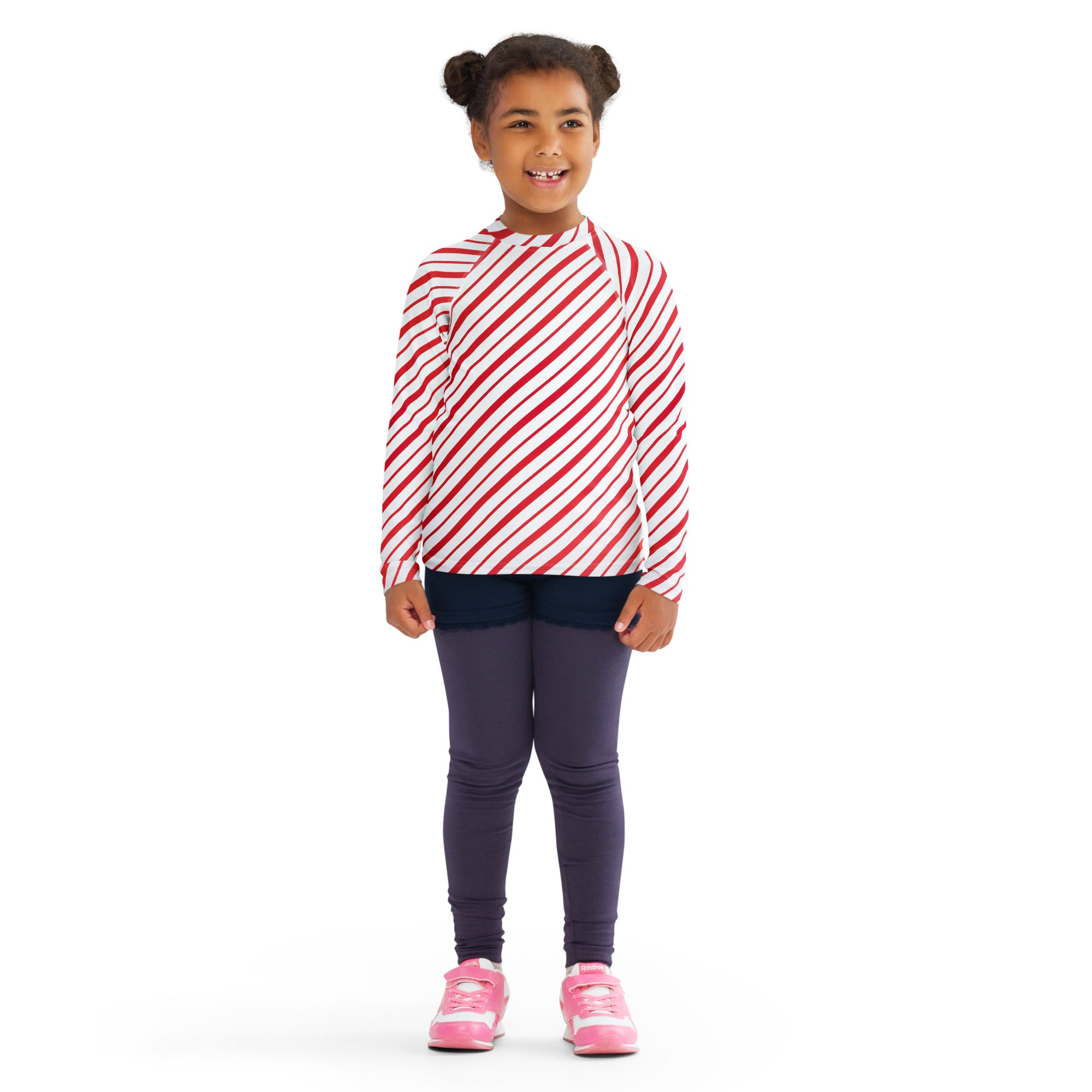 A child wearing a kids red and white candy cane striped long sleeve rash guard swim shirt with UPF 50+ and navy leggings