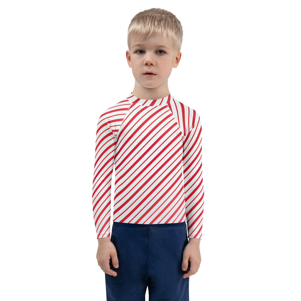 A child wearing a kids red and white candy cane striped long sleeve rash guard swim shirt with UPF 50+ protection