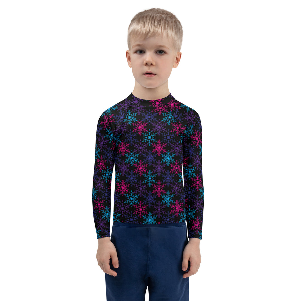 A child wearing a black long sleeve kids neon snowflakes rash guard swim shirt with pink and teal snowflake patterns and UPF 50+