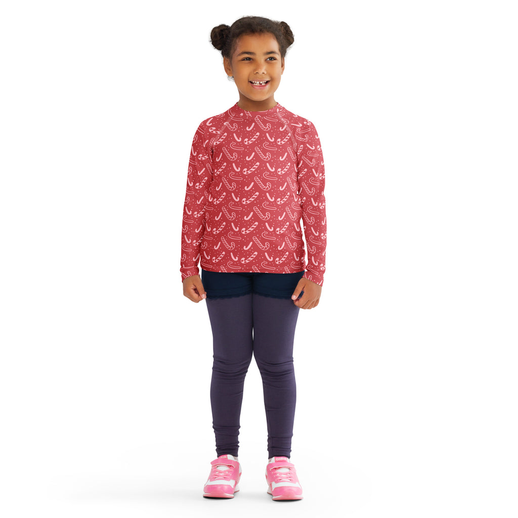 A young girl wearing a kids red candy cane christmas long sleeve rash guard swim shirt with upf 50 and candy cane pattern