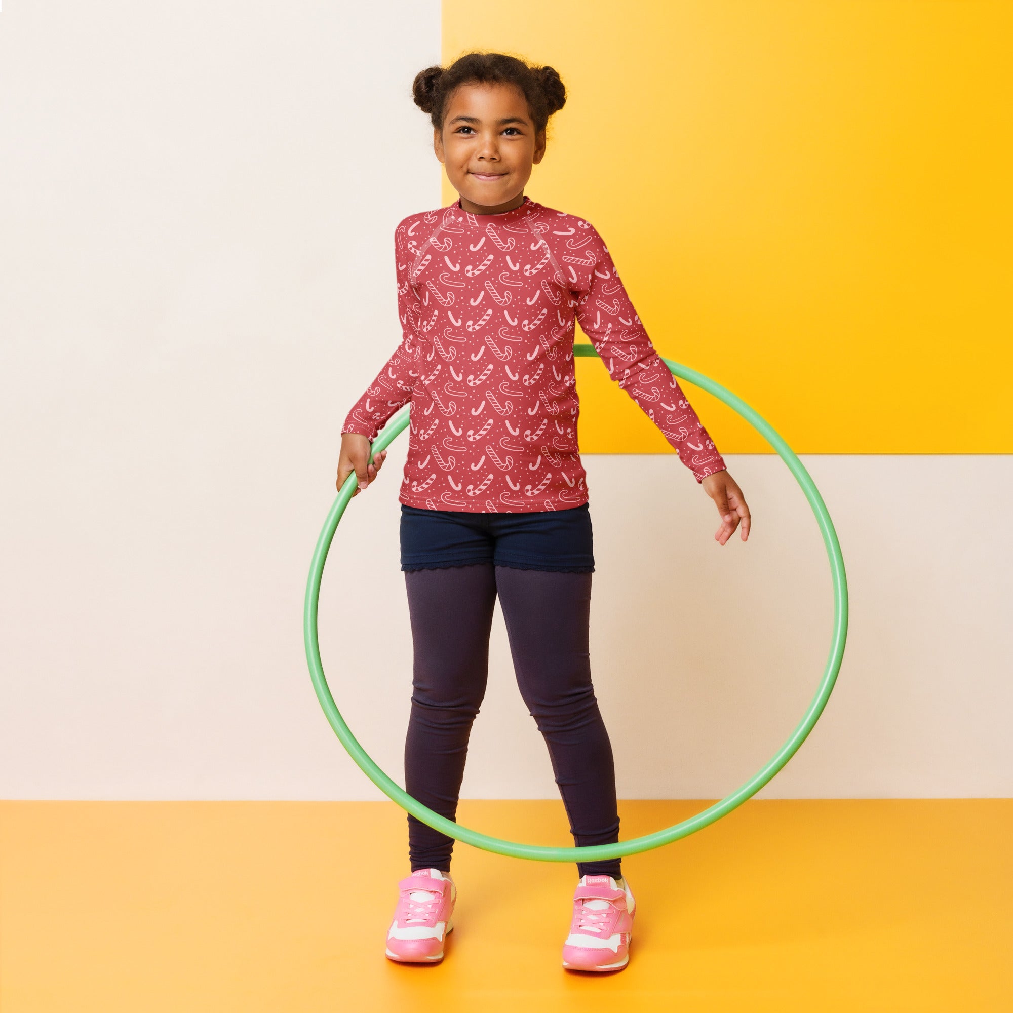 Kids red candy cane Christmas long sleeve rash guard swim shirt with upf 50 plus shown with a green plastic hula hoop