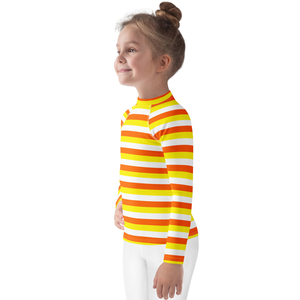 A child wearing a kids candy corn stripes halloween long sleeve rash guard swim shirt with upf 50 plus in bright orange and yellow