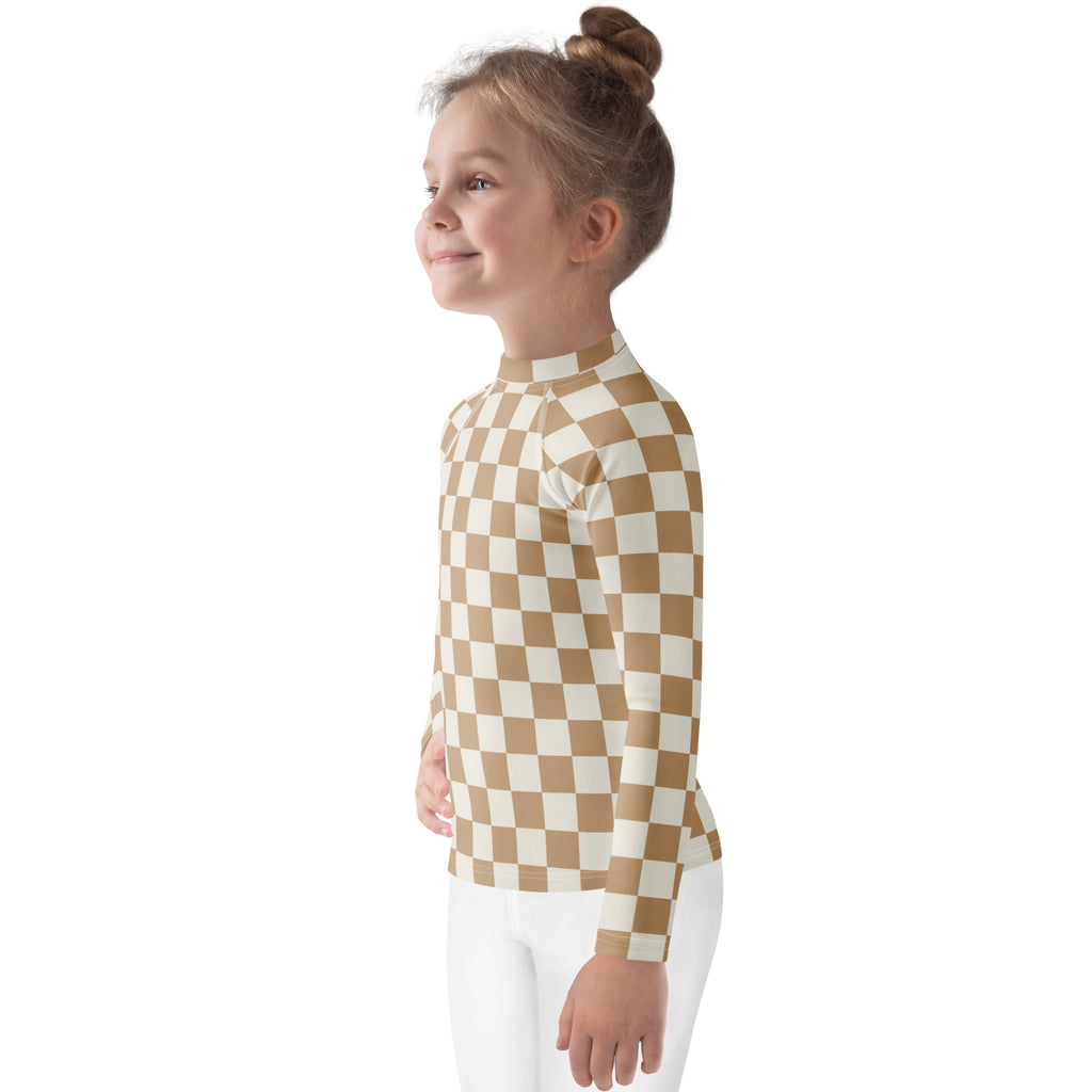 A child wearing a tan and cream checkered kids sand checkerboard long sleeve rash guard swim shirt with UPF 50+