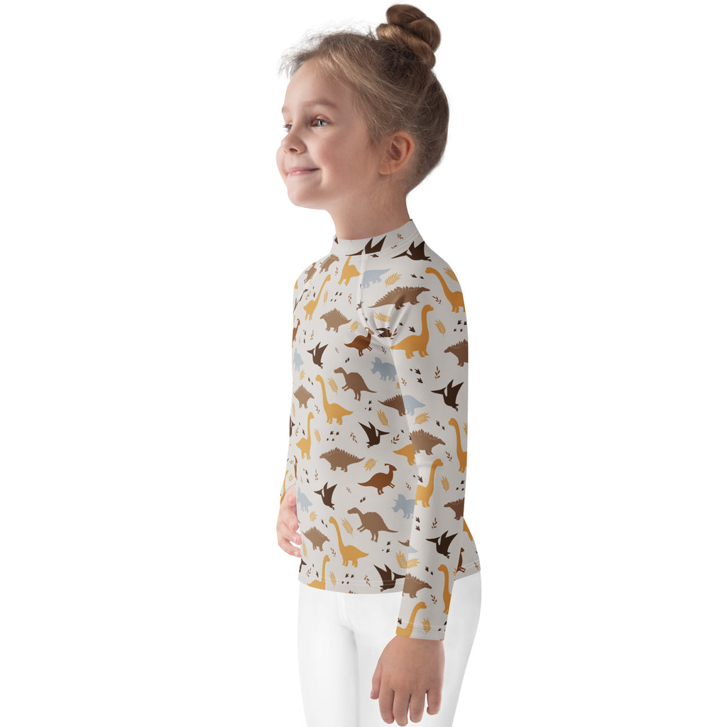 A child wearing a kids dinosaur long sleeve rash guard swim shirt with playful brown yellow gray print and UPF 50+ protection