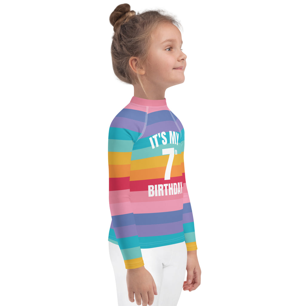 Back of girls bright striped rainbow long sleeve rash guard with its my 7th birthday printed in white and upf 50+