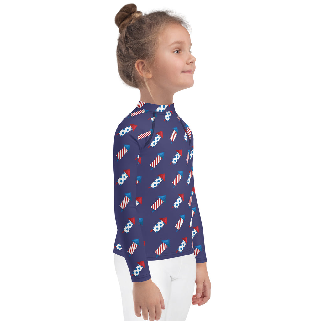 A navy blue kids long sleeve rash guard swim shirt with red white and blue fireworks pattern and UPF 50 plus protection