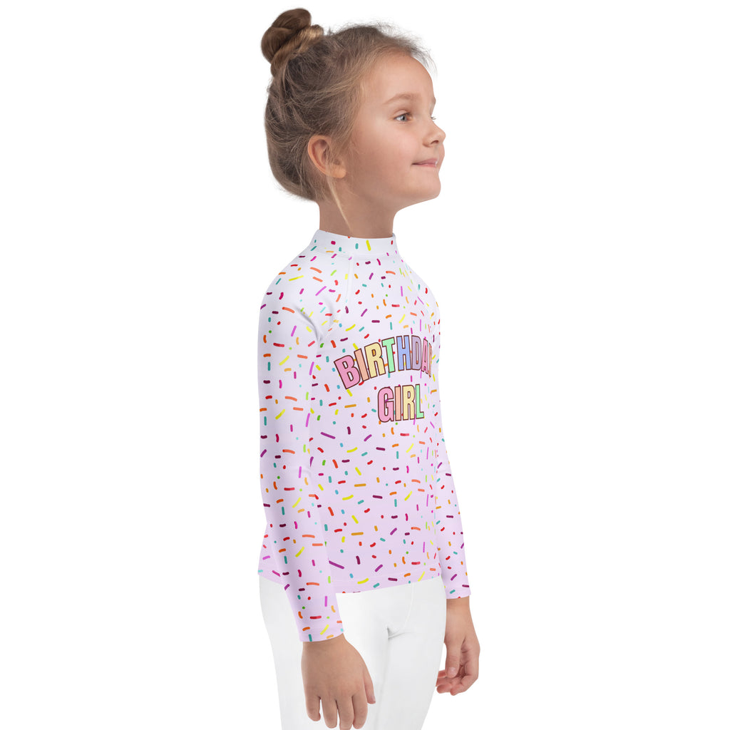 A white long sleeve rash guard swim shirt with colorful sprinkles and rainbow birthday girl text with upf 50+ protection