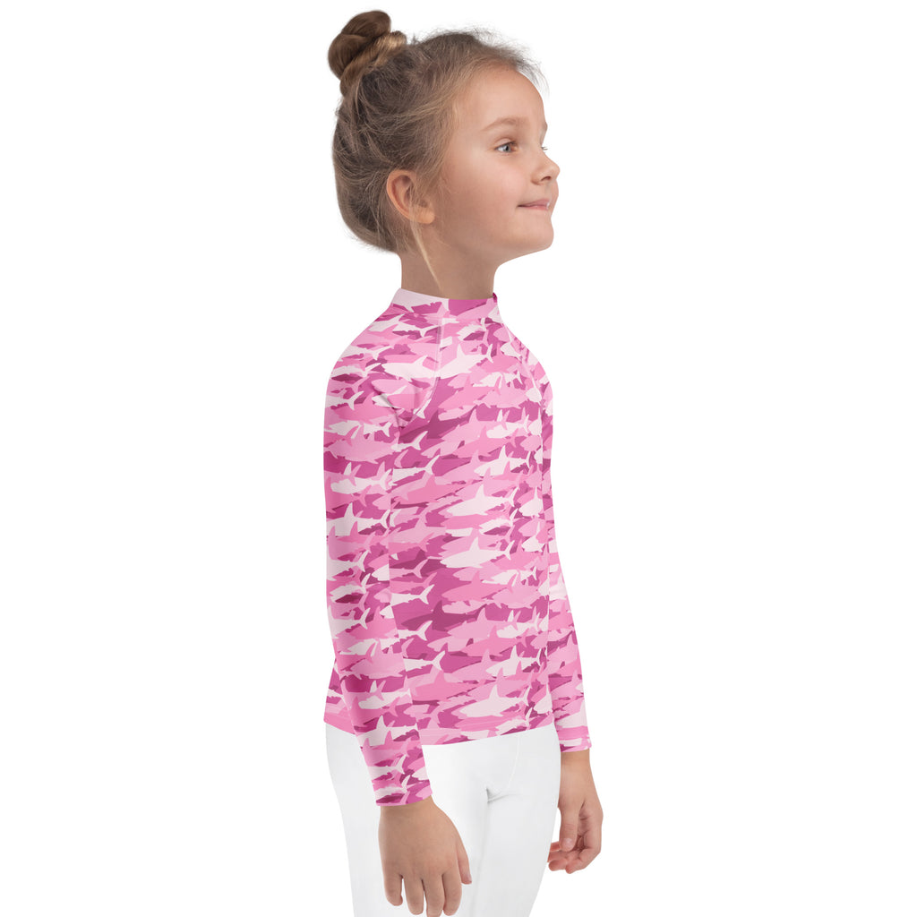 A young girl wearing a pink shark camouflage long sleeve rash guard swim shirt with UPF 50 plus protection