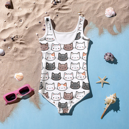 Kids swimsuit with cute cat face print, displayed on sandy beach with seashells and sunglasses.