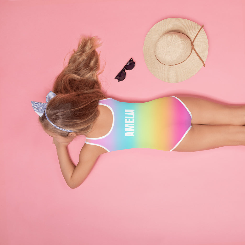 Back side of a girls bright rainbow one-piece swimsuit with white trim and the name amelia printed on the back