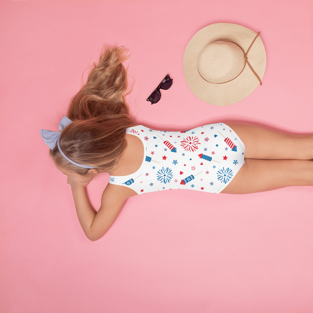 Girls white buttery soft one-piece swimsuit with red blue star fireworks pattern for 4th of July celebration