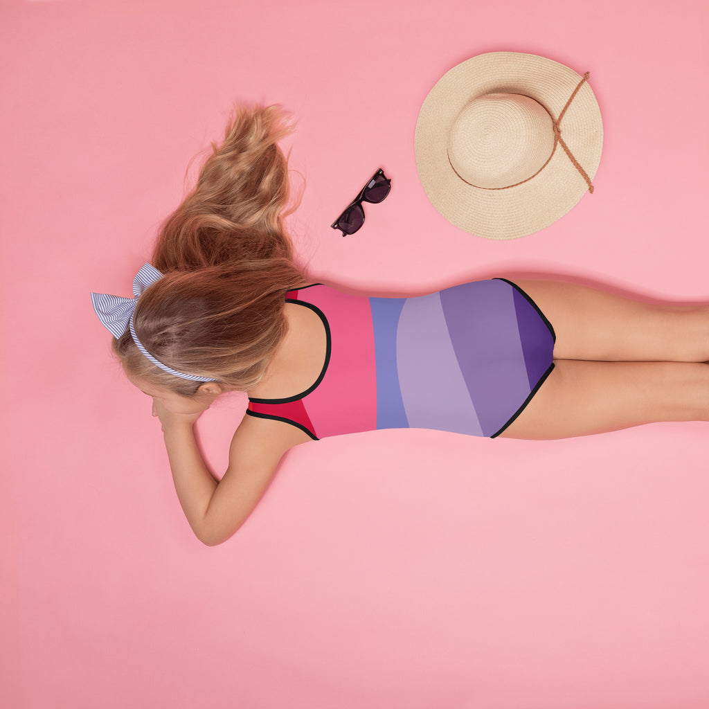 A girl wearing a vibrant red purple and pink striped girls abstract waves one piece swimsuit with upf 50+ protection