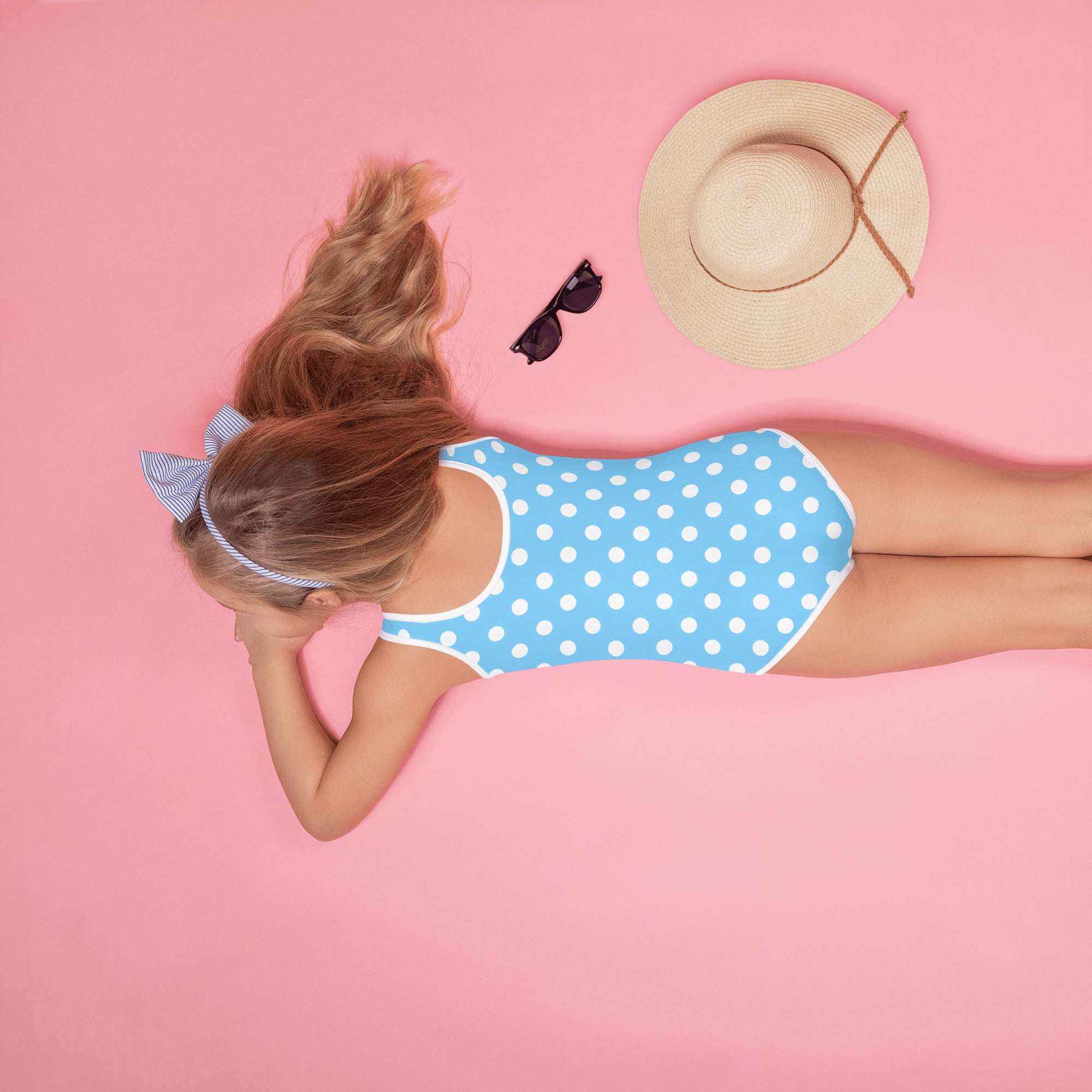 A girl wearing a girls blue polka dots buttery soft swimsuit with upf 50 plus and a matching striped headband