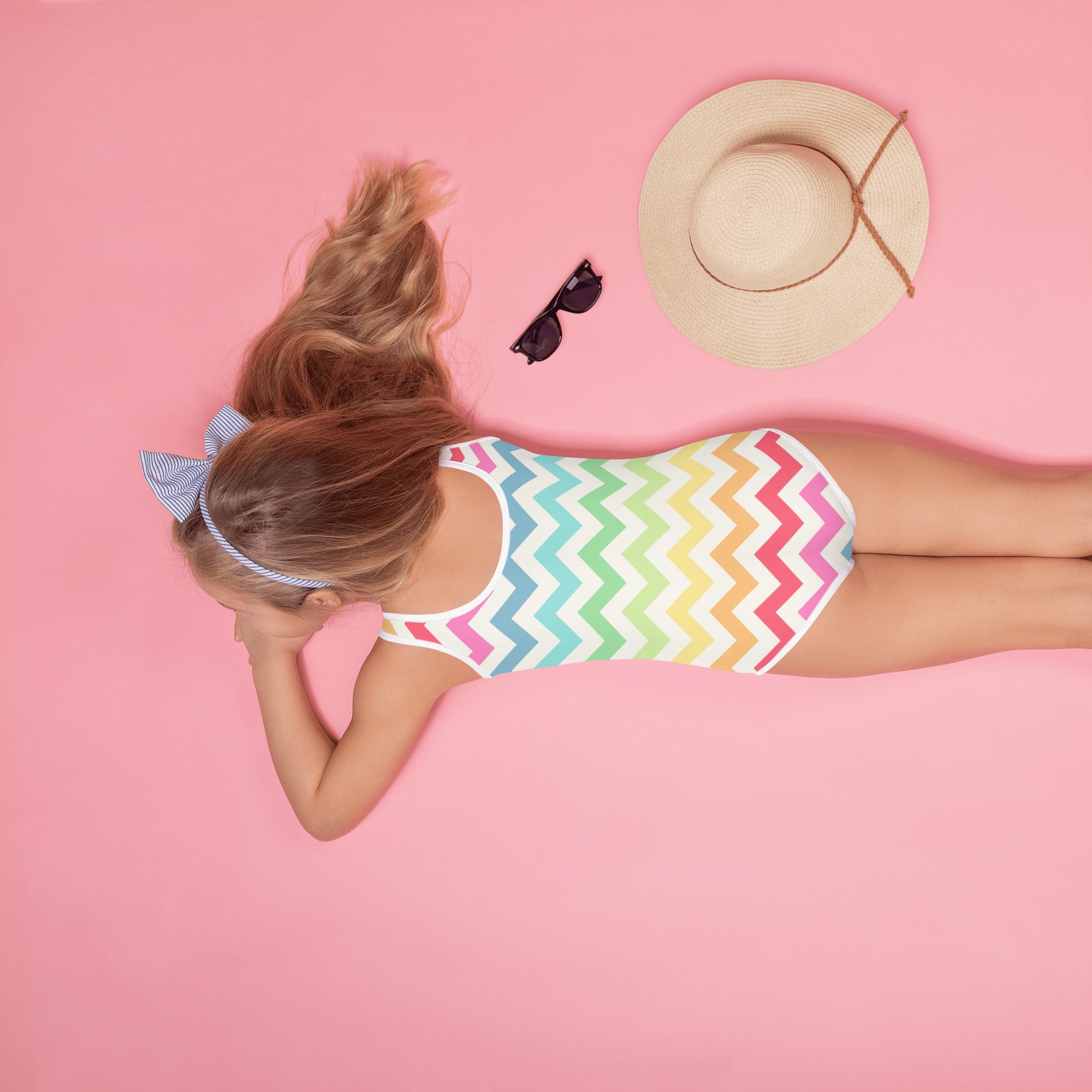 A girl wearing a girls pastel rainbow chevron buttery soft swimsuit with upf 50 plus and a blue striped headband
