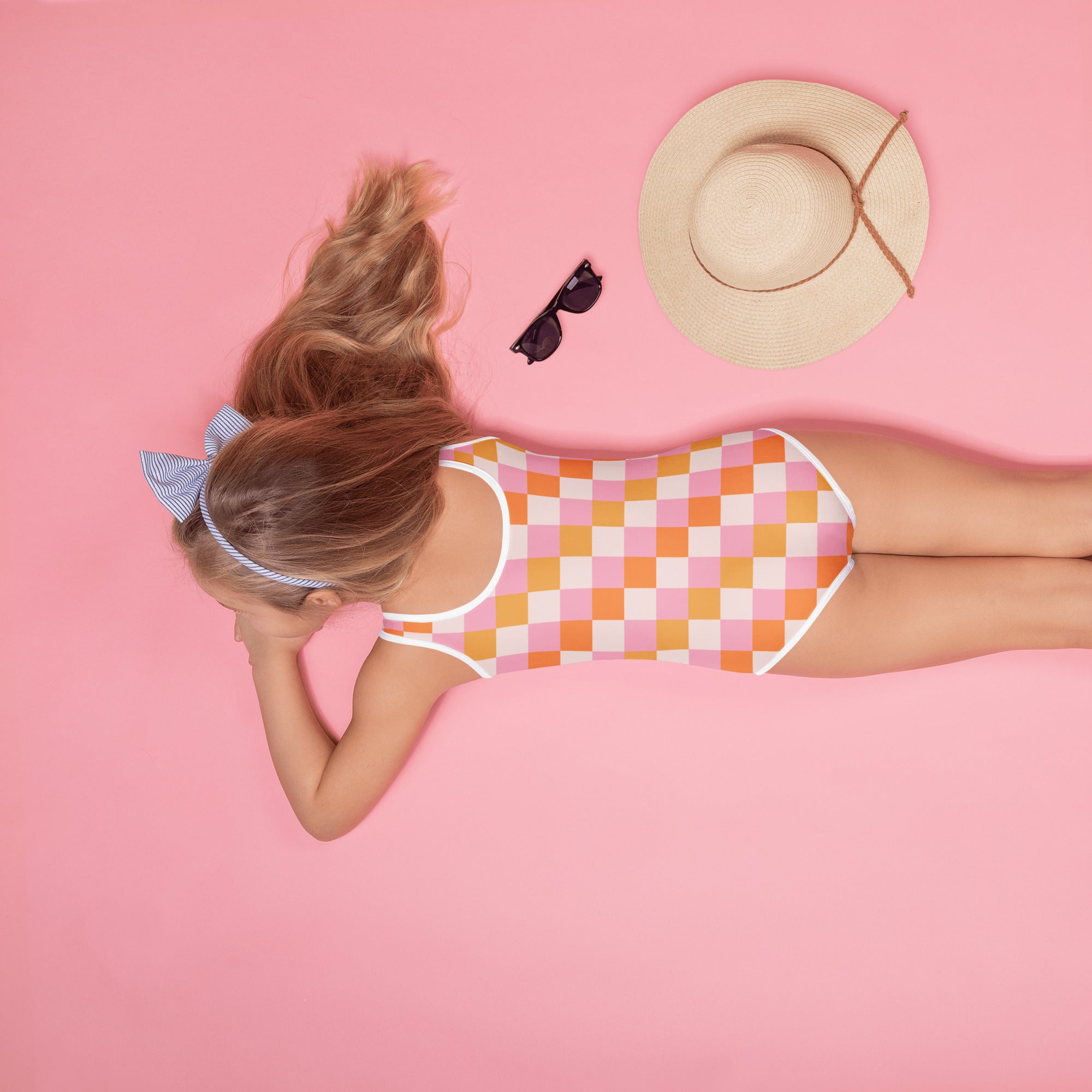 A girl wearing a girls pink and orange checkered buttery soft swimsuit with upf 50 plus and white trim