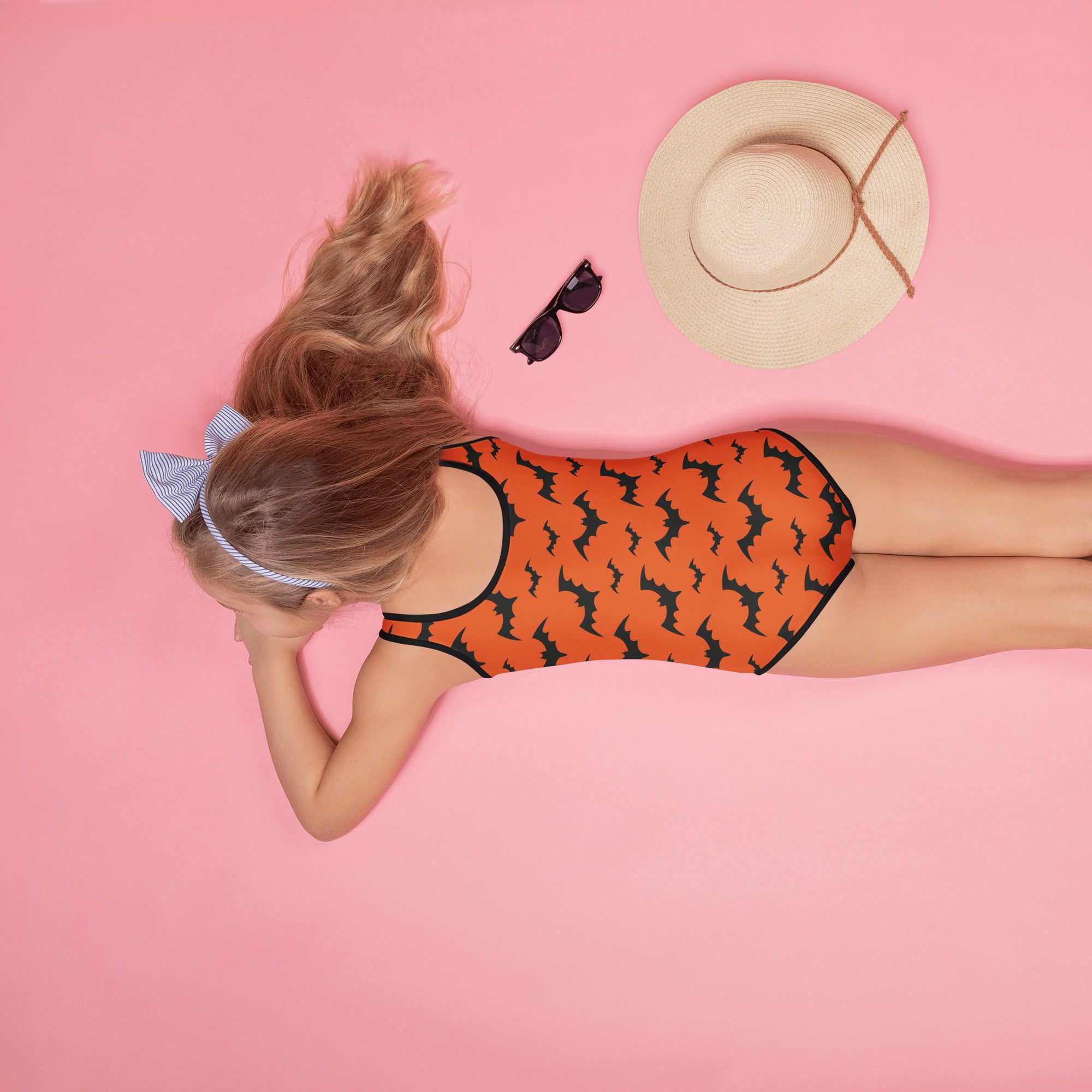 Girls orange one-piece swimsuit with black bat pattern and trim made of buttery soft fabric with UPF 50 plus protection