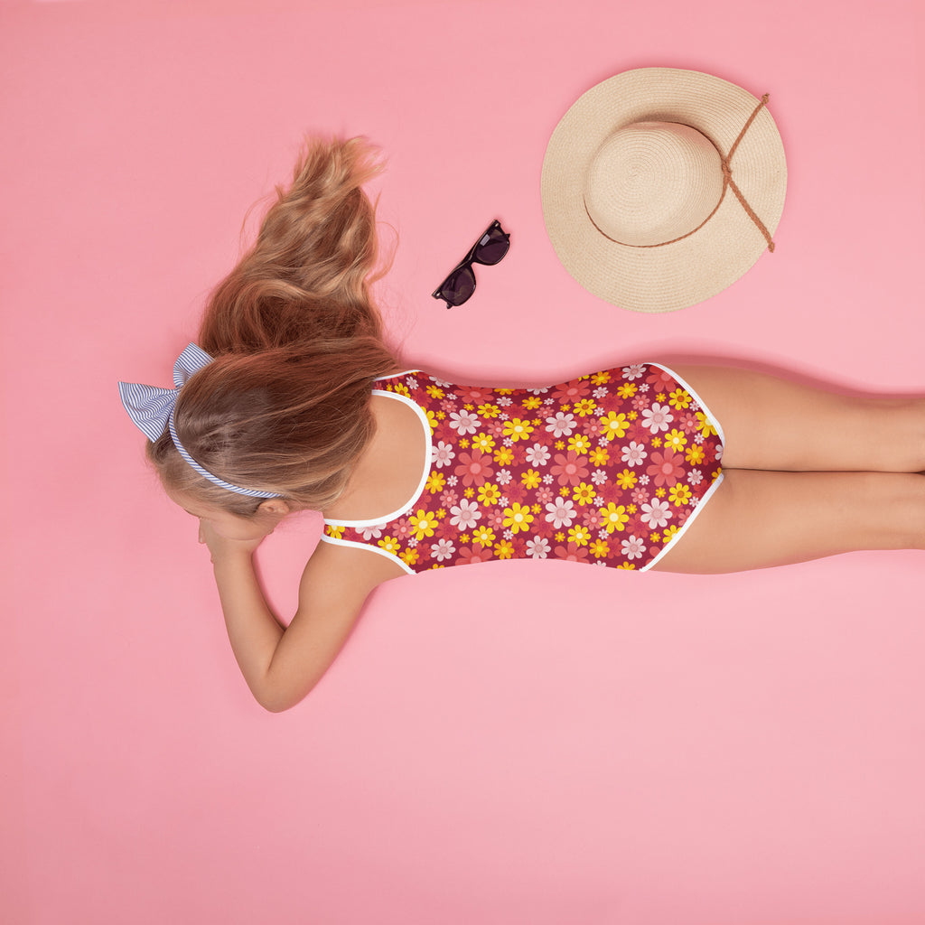 A girl wearing a girls red daisy buttery soft one-piece swimsuit with upf 50 plus in red yellow and pink floral design with white trim
