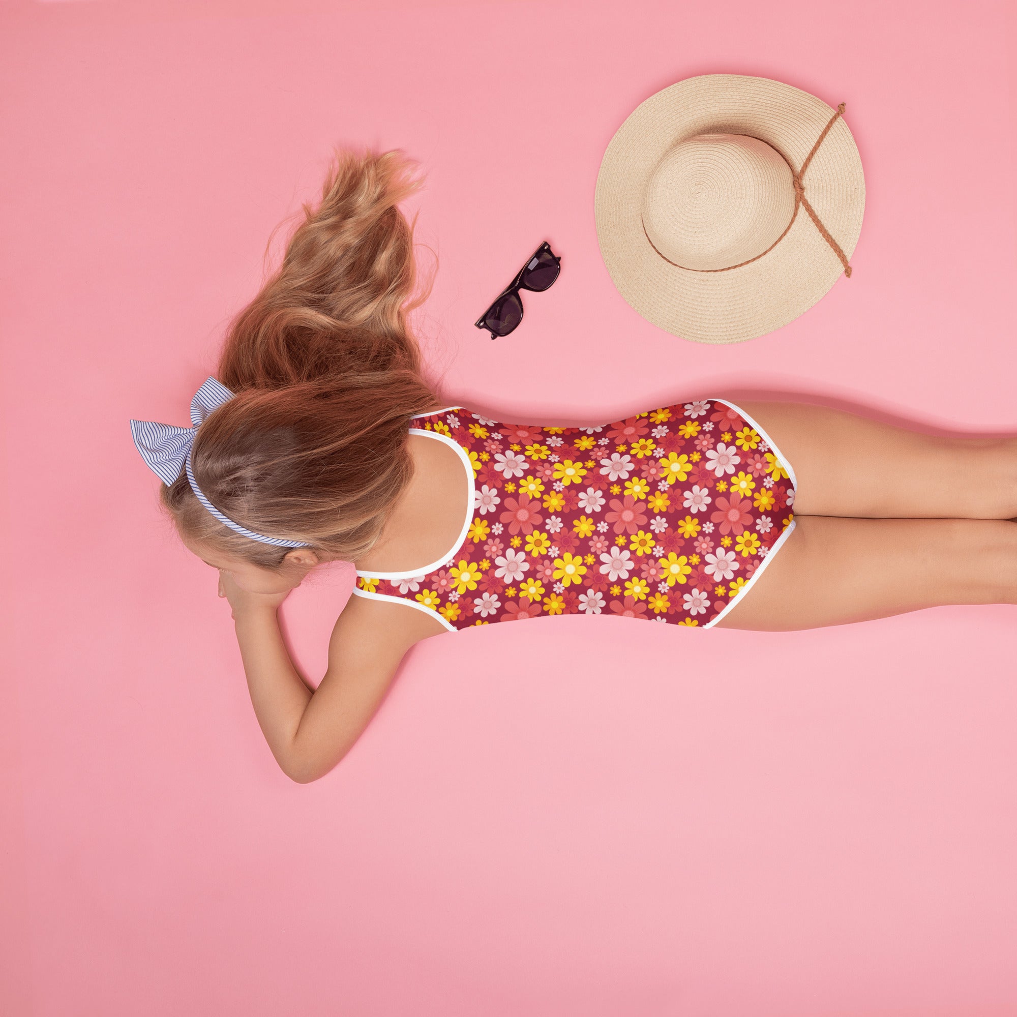 A girl wearing a girls red daisy buttery soft one-piece swimsuit with upf 50 plus in red yellow and pink floral design with white trim