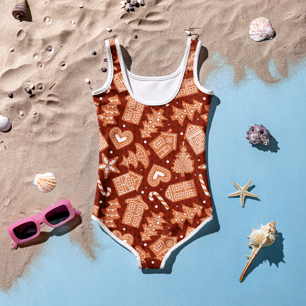 A festive brown girls one-piece swimsuit with white trim and gingerbread house candy cane snowflake patterns with upf 50+