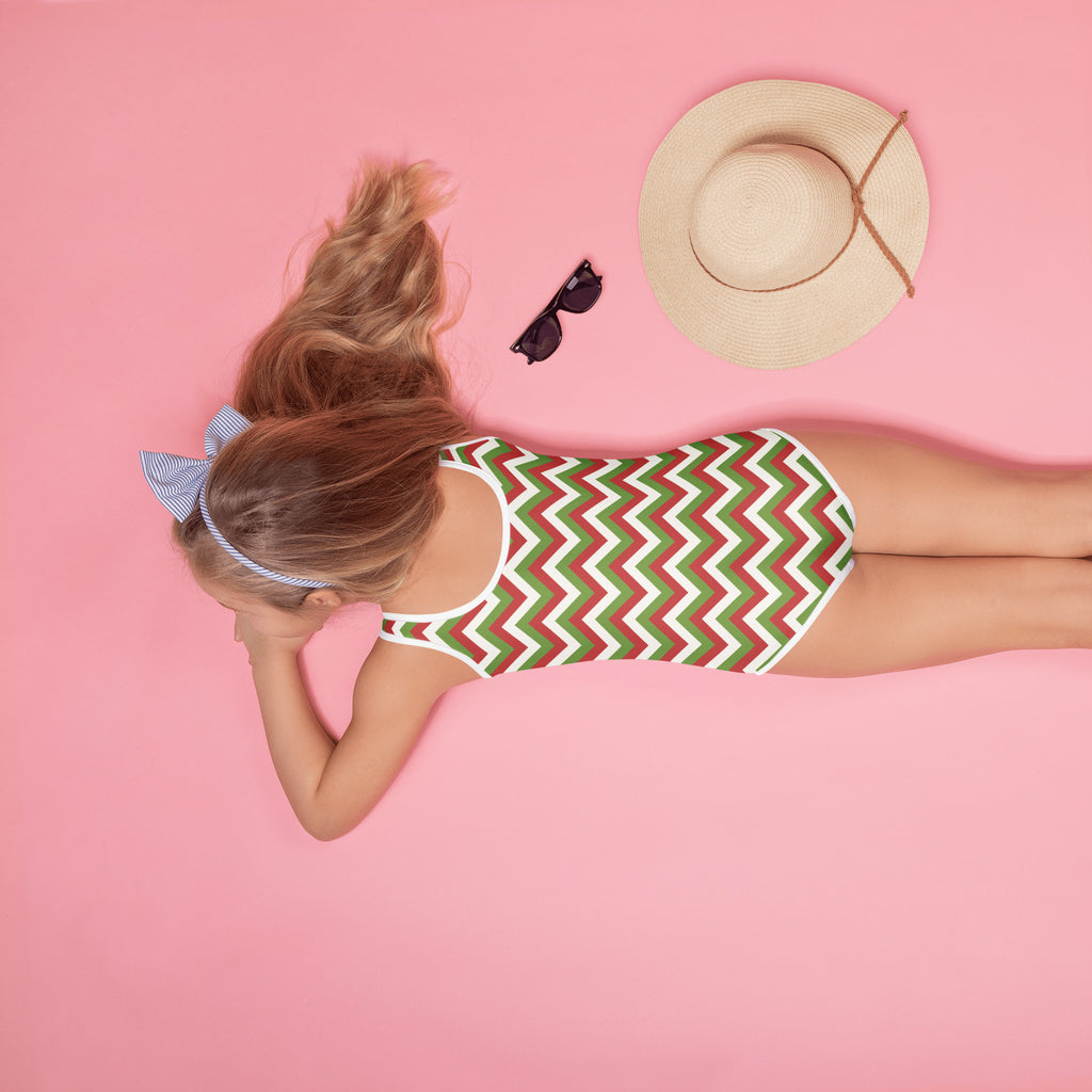 A girl wearing a girls christmas chevron buttery soft swimsuit with red green white zigzag pattern and UPF 50+ protection