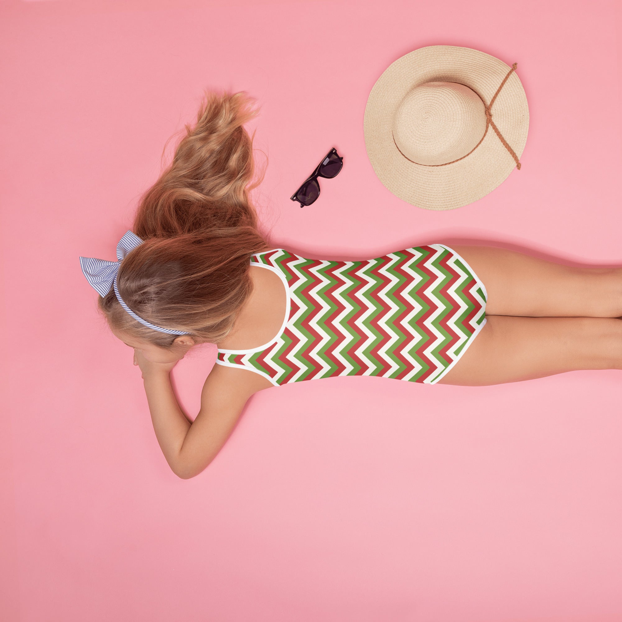 A girl wearing a girls christmas chevron buttery soft swimsuit with red green white zigzag pattern and UPF 50+ protection