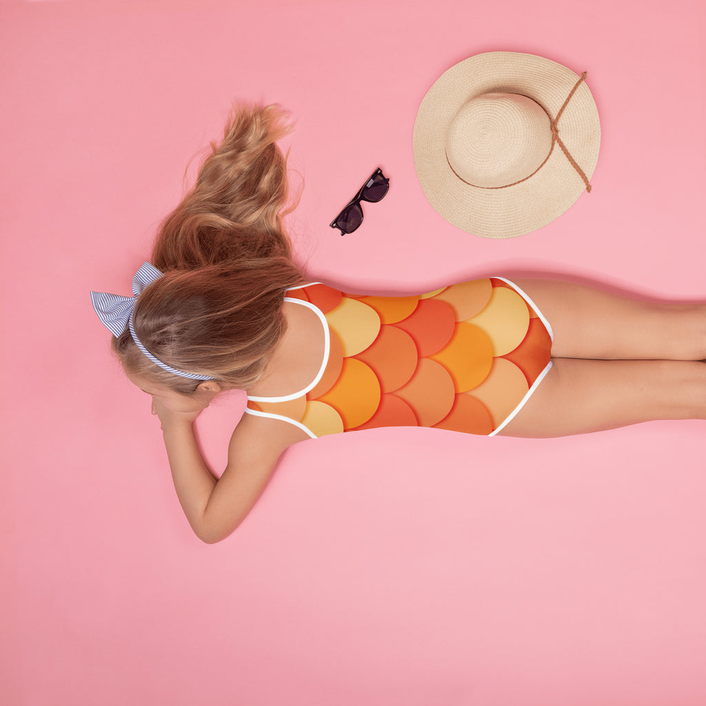 A girl wearing an orange and yellow fish-scale girls mermaid buttery soft swimsuit with white trim and UPF 50+ protection