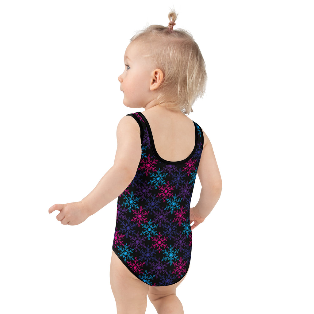 A toddler wearing a black neon snowflake buttery soft girls swimsuit with upf 50 plus in pink and blue patterns