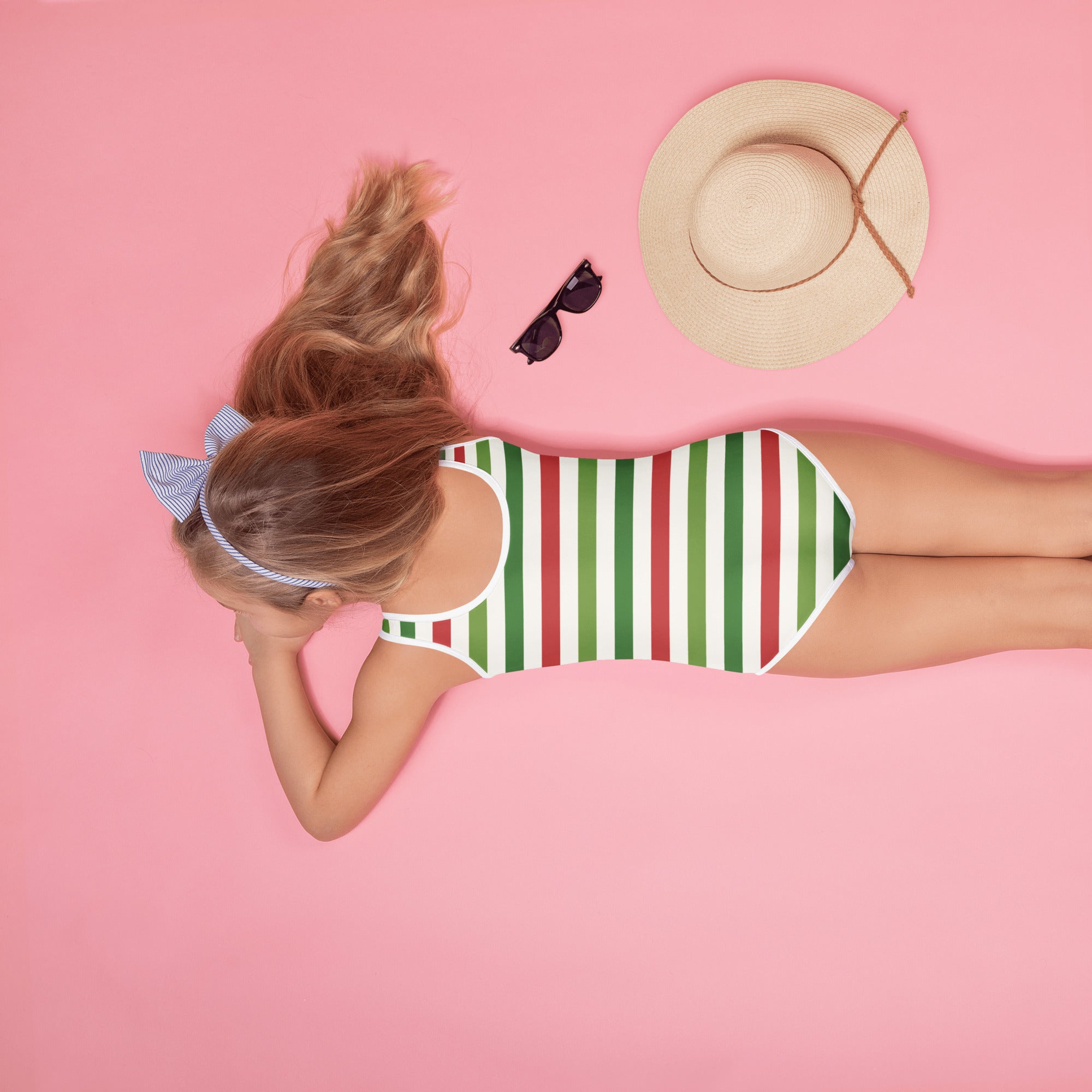 A girl wearing a girls striped Christmas buttery soft one-piece swimsuit with UPF 50+ and a blue-and-white headband