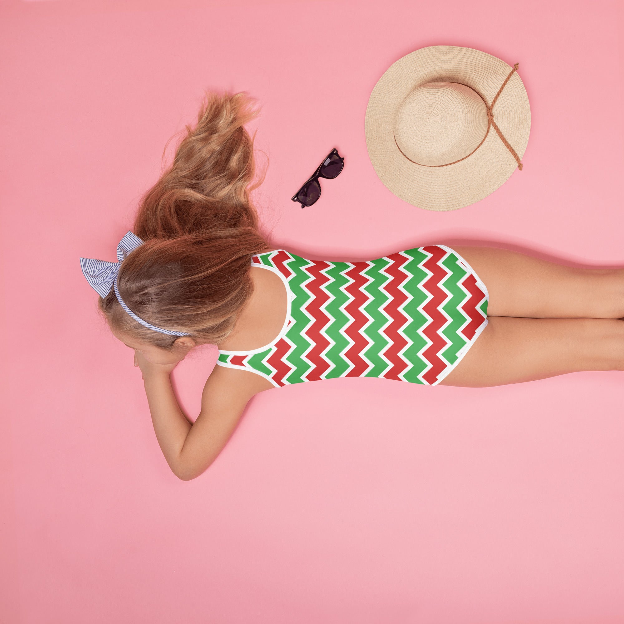 A girl wearing a girls chevron christmas buttery soft one-piece swimsuit with red and green zigzag patterns and UPF 50+