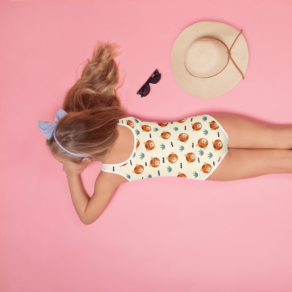 A child wearing a white girls tiger print buttery soft swimsuit with orange tiger and green leaf patterns and UPF 50+