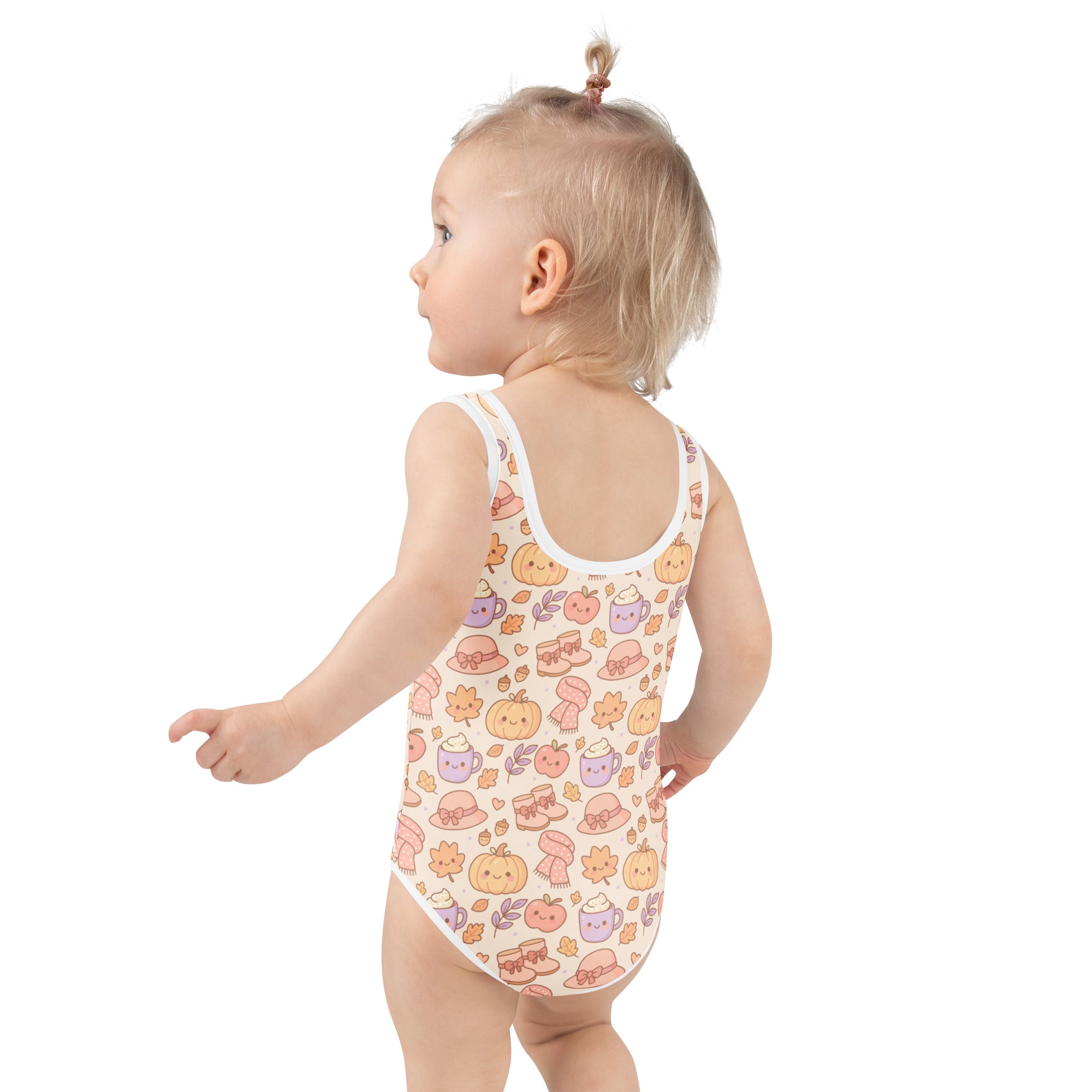 A toddler wearing a cream cozy fall themed buttery soft swimsuit with cartoon pumpkins hats and coffee cups pattern