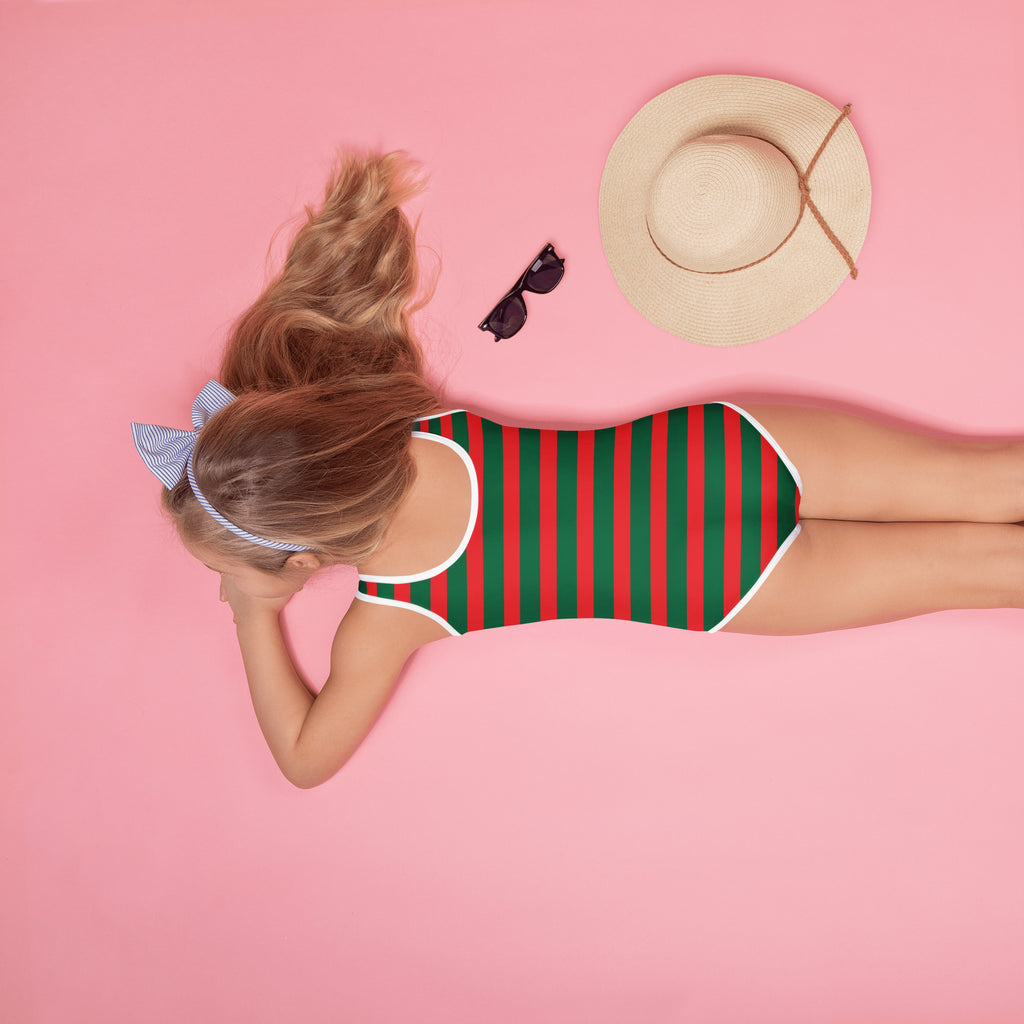 A girl wearing a girls festive christmas stripes buttery soft red and green striped swimsuit with upf 50+
