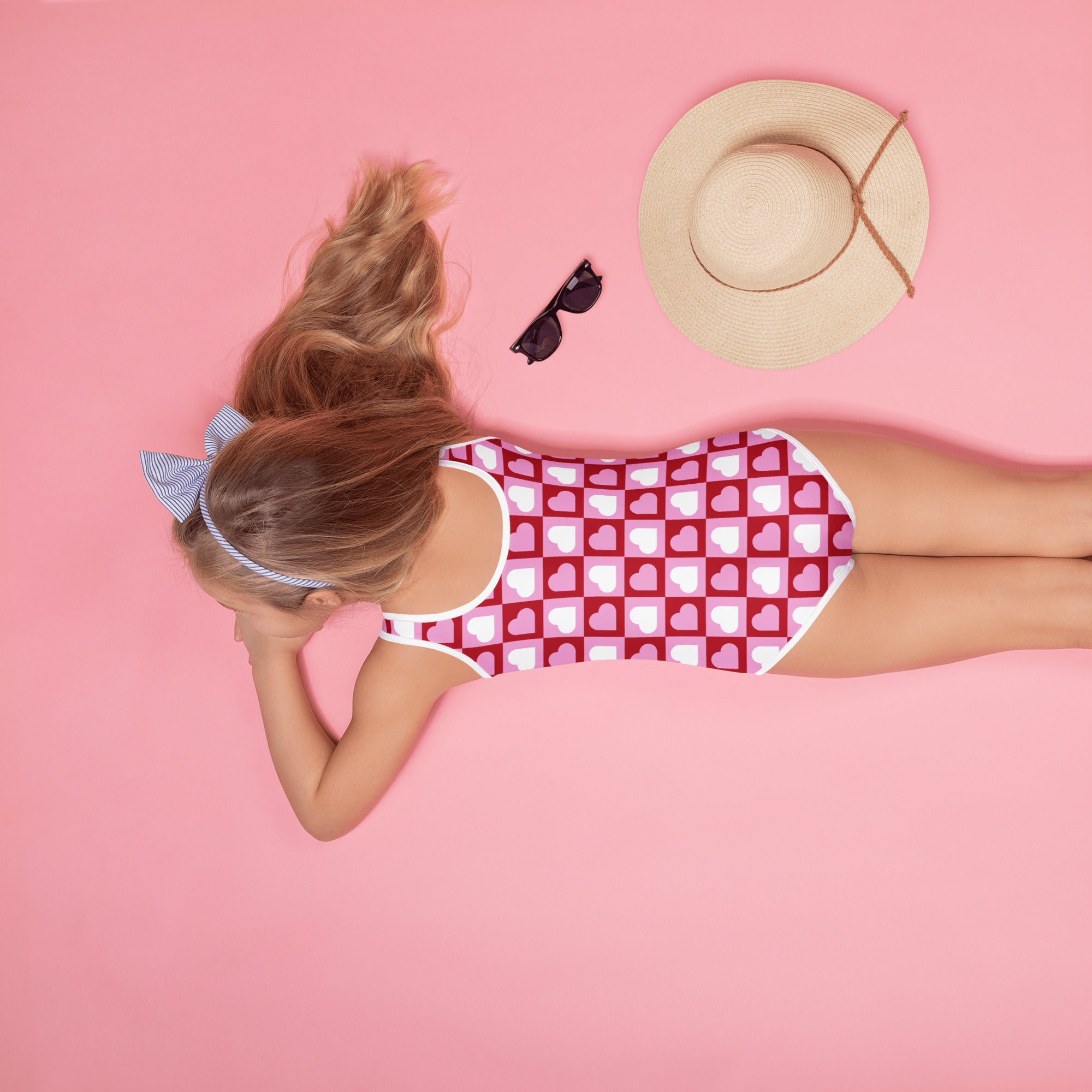 A girl wearing a girls pink heart squares checkerboard buttery soft swimsuit with upf 50 plus and thin straps
