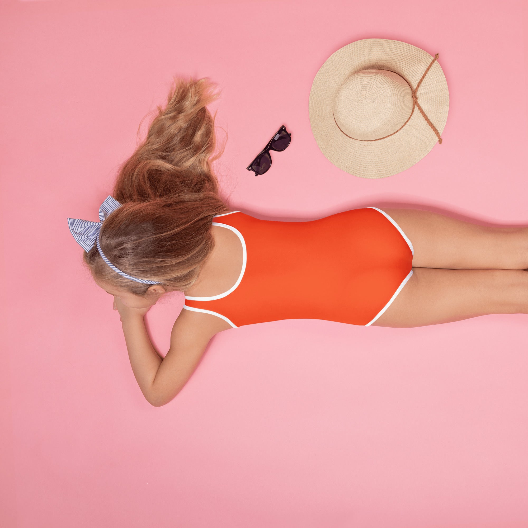 A vibrant orange girls one-piece swimsuit with white trim and buttery soft fabric lying on a pink surface