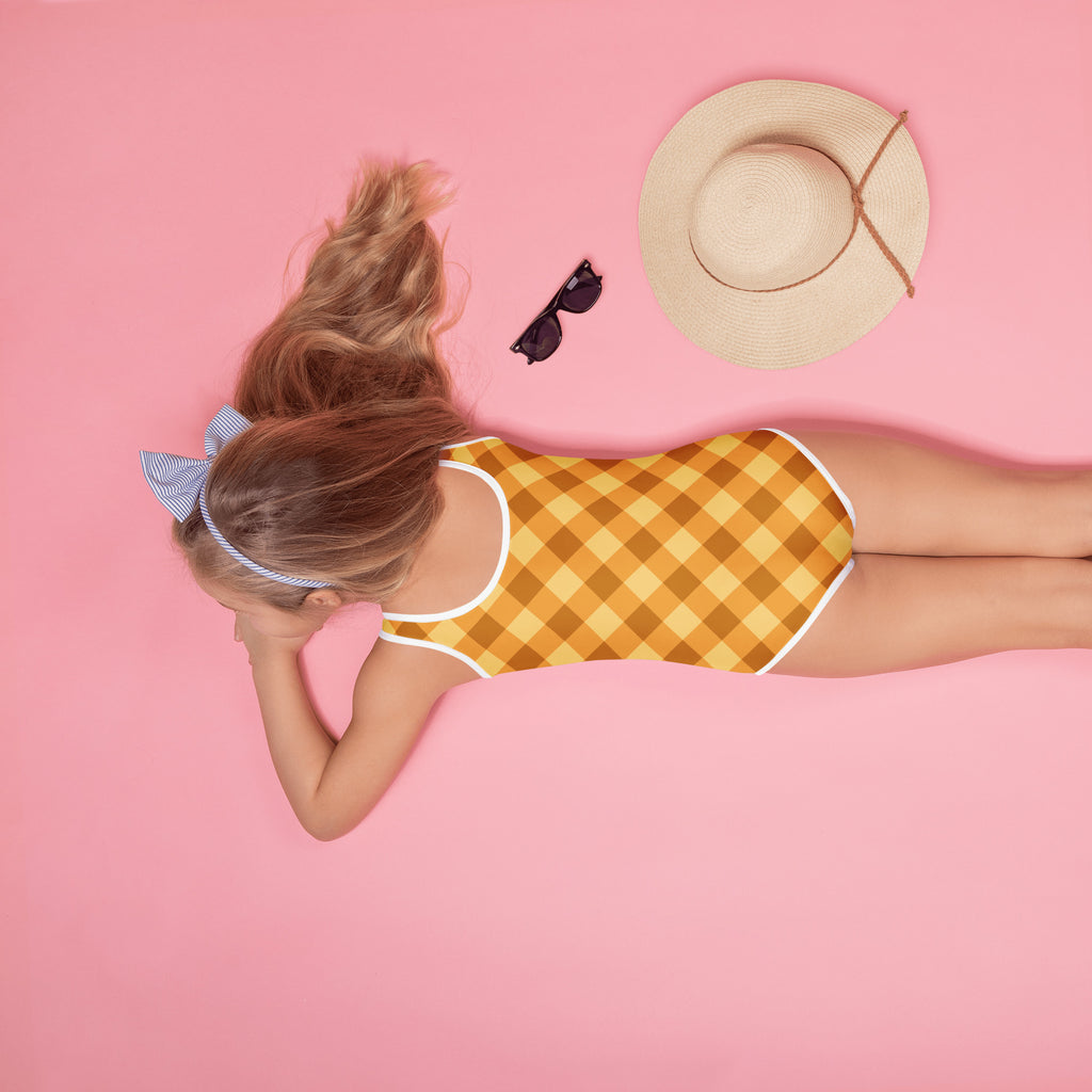 A girl wearing a girls golden gingham buttery soft yellow and brown checkered swimsuit with white trim and UPF 50+ protection