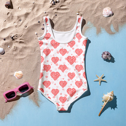 White girls crystal heart buttery soft one-piece swimsuit with pink geometric pattern and upf 50 plus on sandy beach