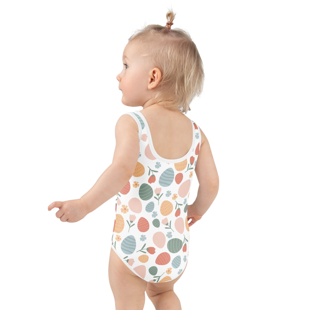 A toddler wearing a white girls pastel easter egg pattern buttery soft swimsuit with upf 50 plus and double layered front