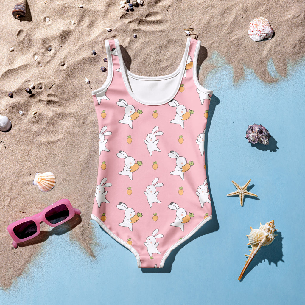 Pink swimsuit with bunny pattern on a sandy and blue gradient background with shells and sunglasses.
