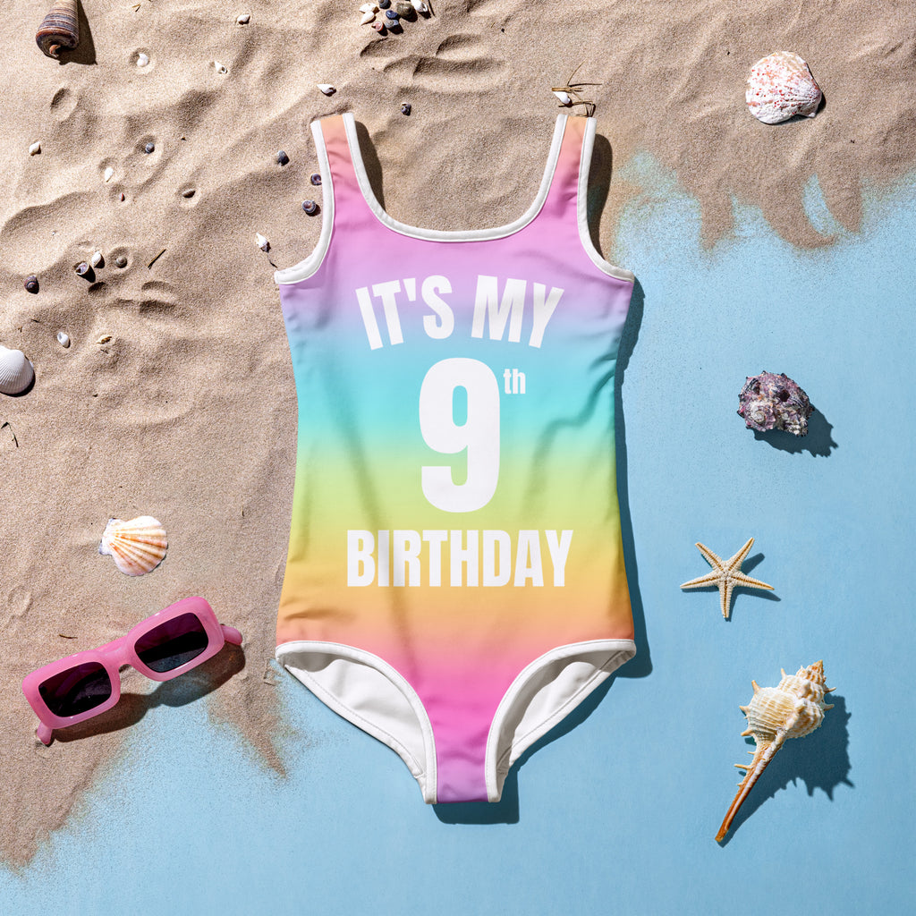 A vibrant rainbow gradient one-piece swimsuit with white trim and its my 9th birthday text printed on front
