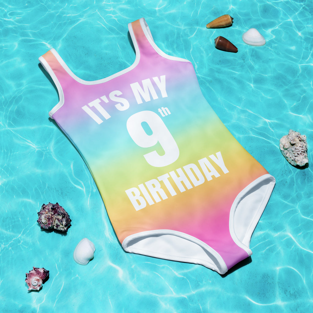 A vibrant rainbow one-piece girls swimsuit with white trim and its my 9th birthday printed in bold white letters