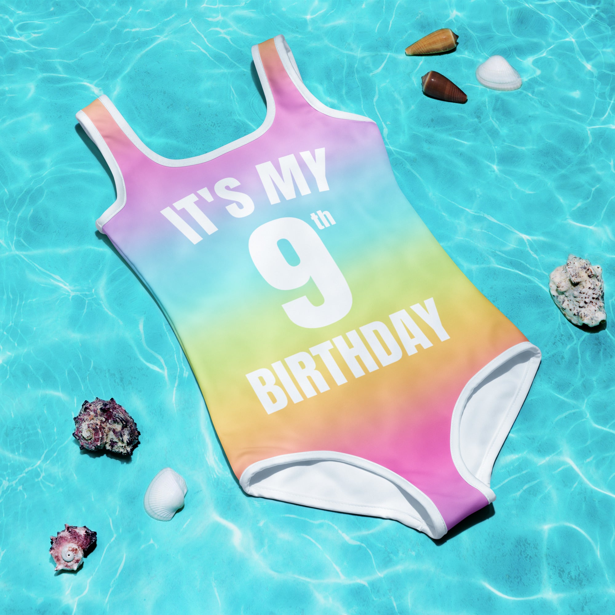 A vibrant rainbow one-piece girls swimsuit with white trim and its my 9th birthday printed in bold white letters