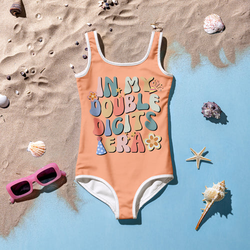 Girls coral one-piece swimsuit with white trim and multicolored in my double digits era graphic for 10th birthday