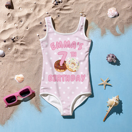 Pink polka-dot girls one-piece swimsuit with emmas 7th birthday and donut graphics for custom name and age